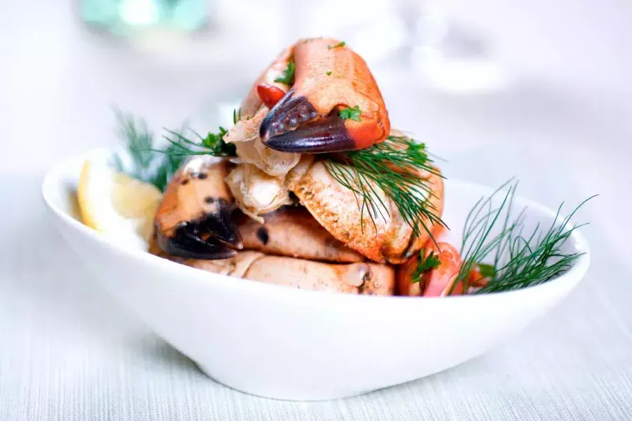 Crab legs are stacked in a white bowl 和 sprinkled with fresh dill.